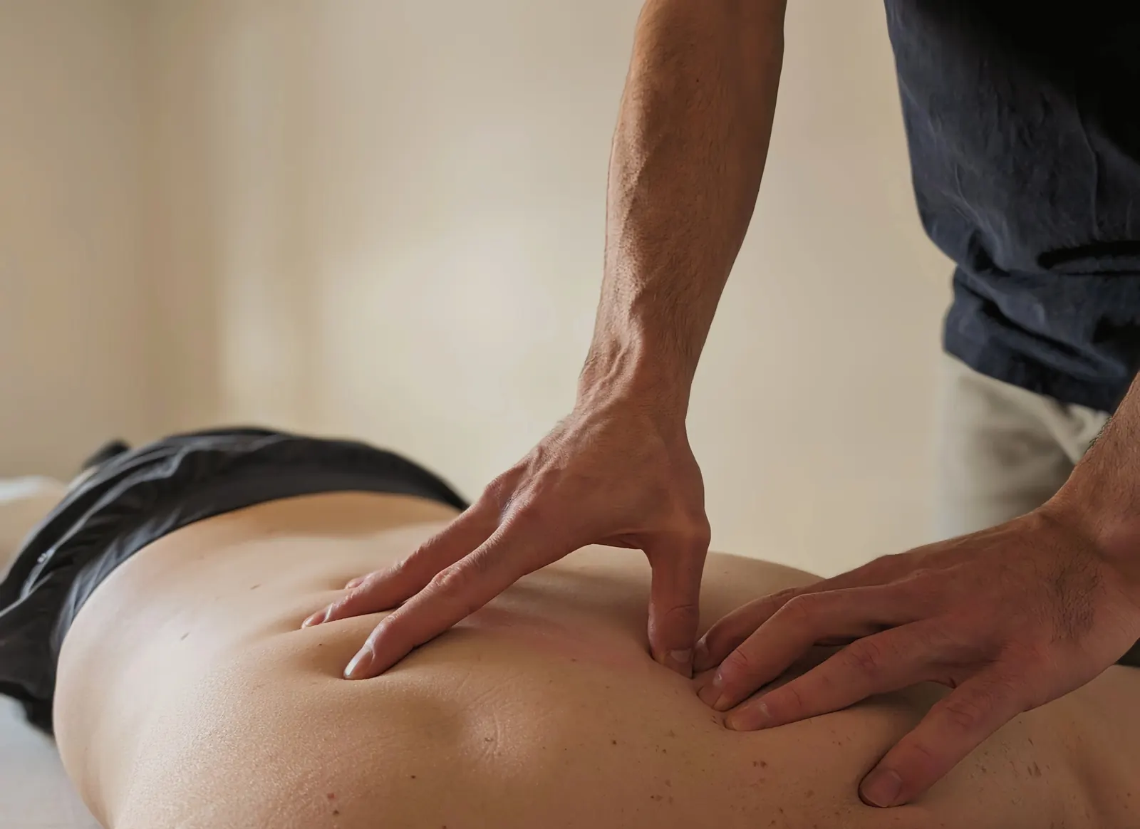 Gros plan sur les mains de l'ostéopathe exerçant une pression ciblée sur le dos d'un patient.
